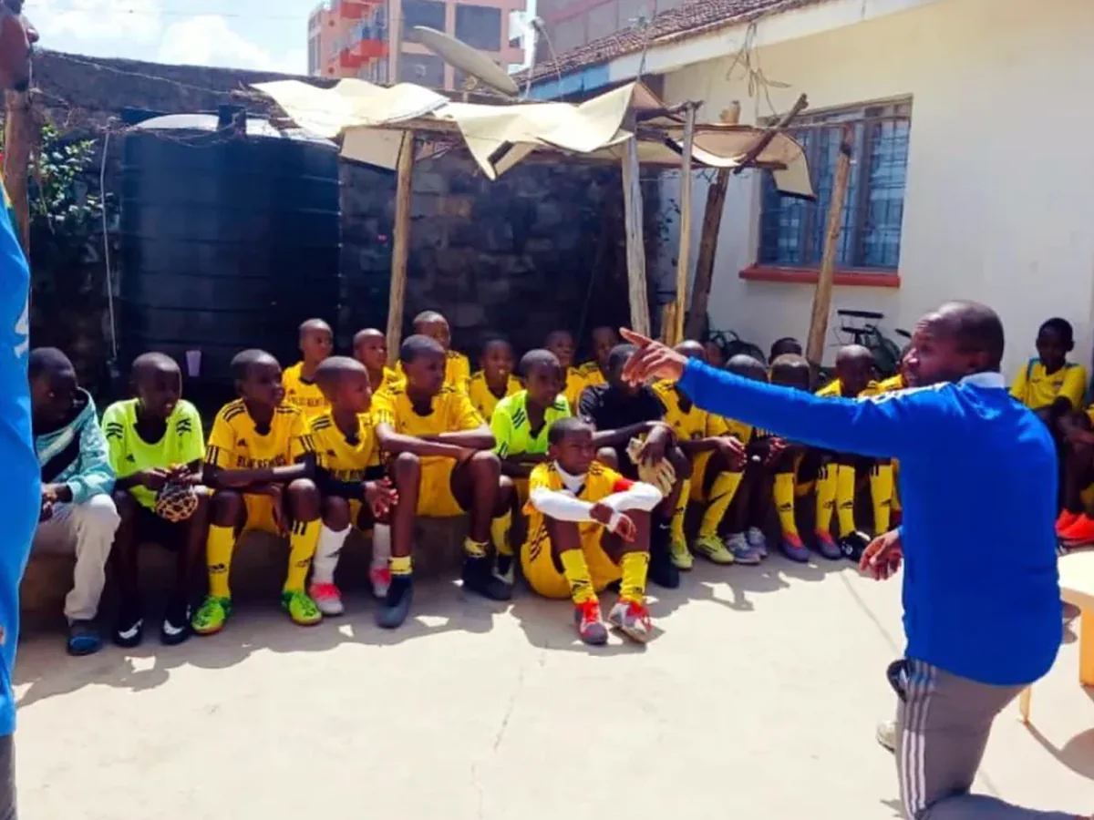 Coach addressing young players in yellow kits at a community training session
